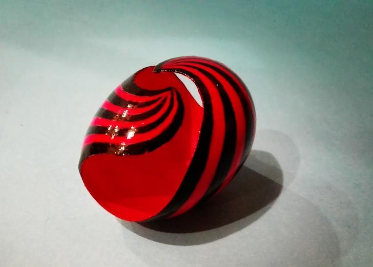 Egg decorated with red and black paint, carved with a spiral pattern creating a dynamic and modern effect.