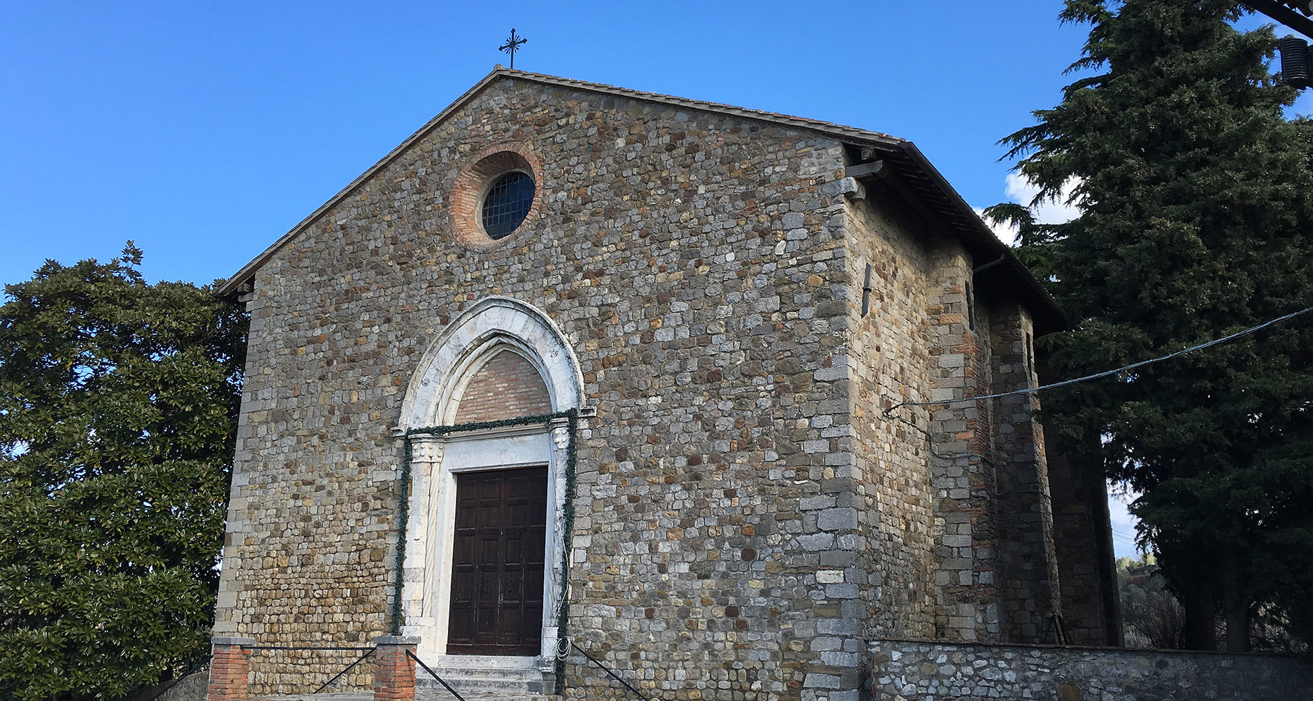 Façade en pierre de l’église Santa Maria Vecchia à Ficulle, avec un portail gothique et une petite rosace circulaire.