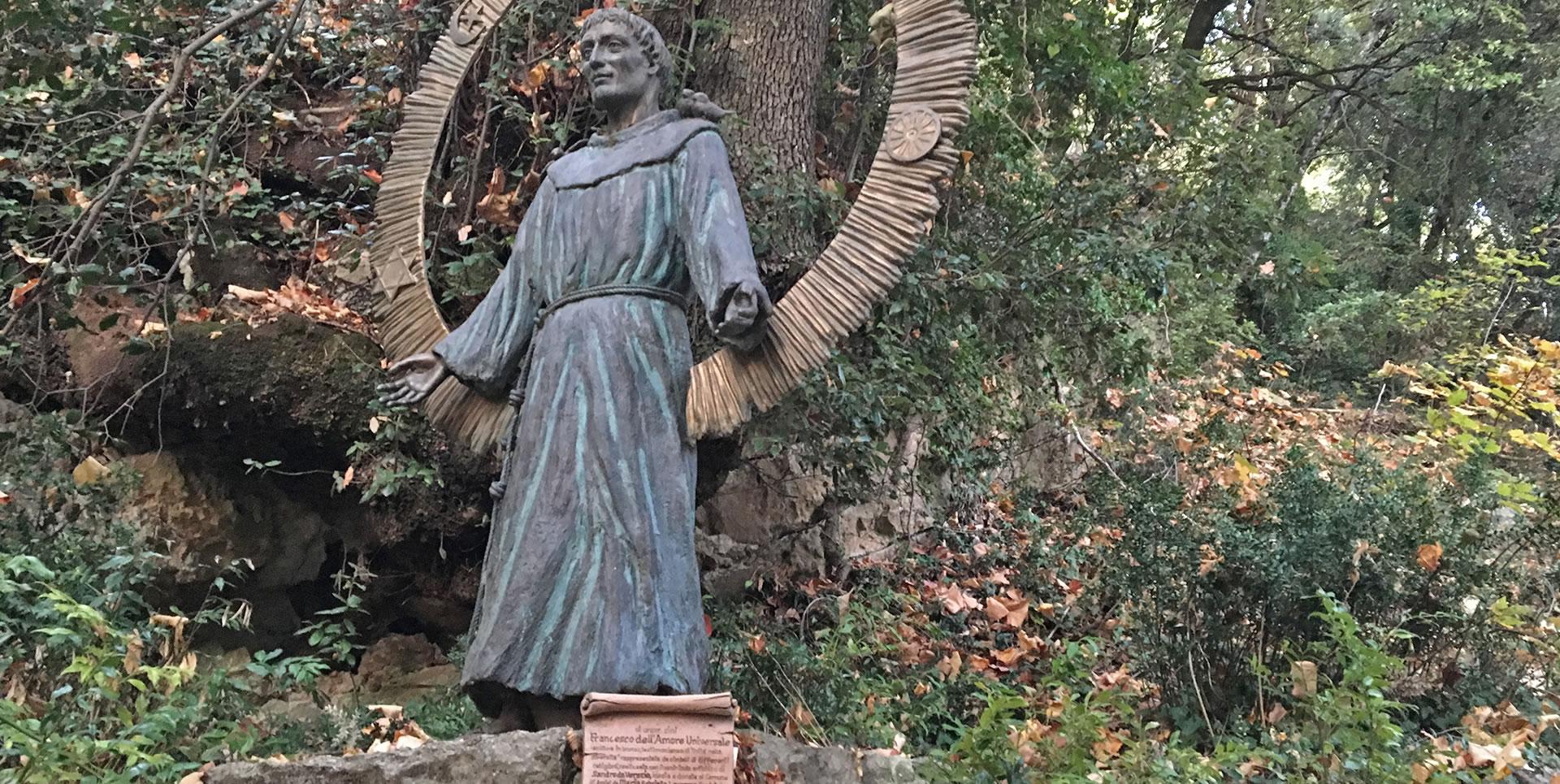 Statue de Saint François, immergée dans la nature, les bras ouverts en signe d’accueil et de spiritualité.