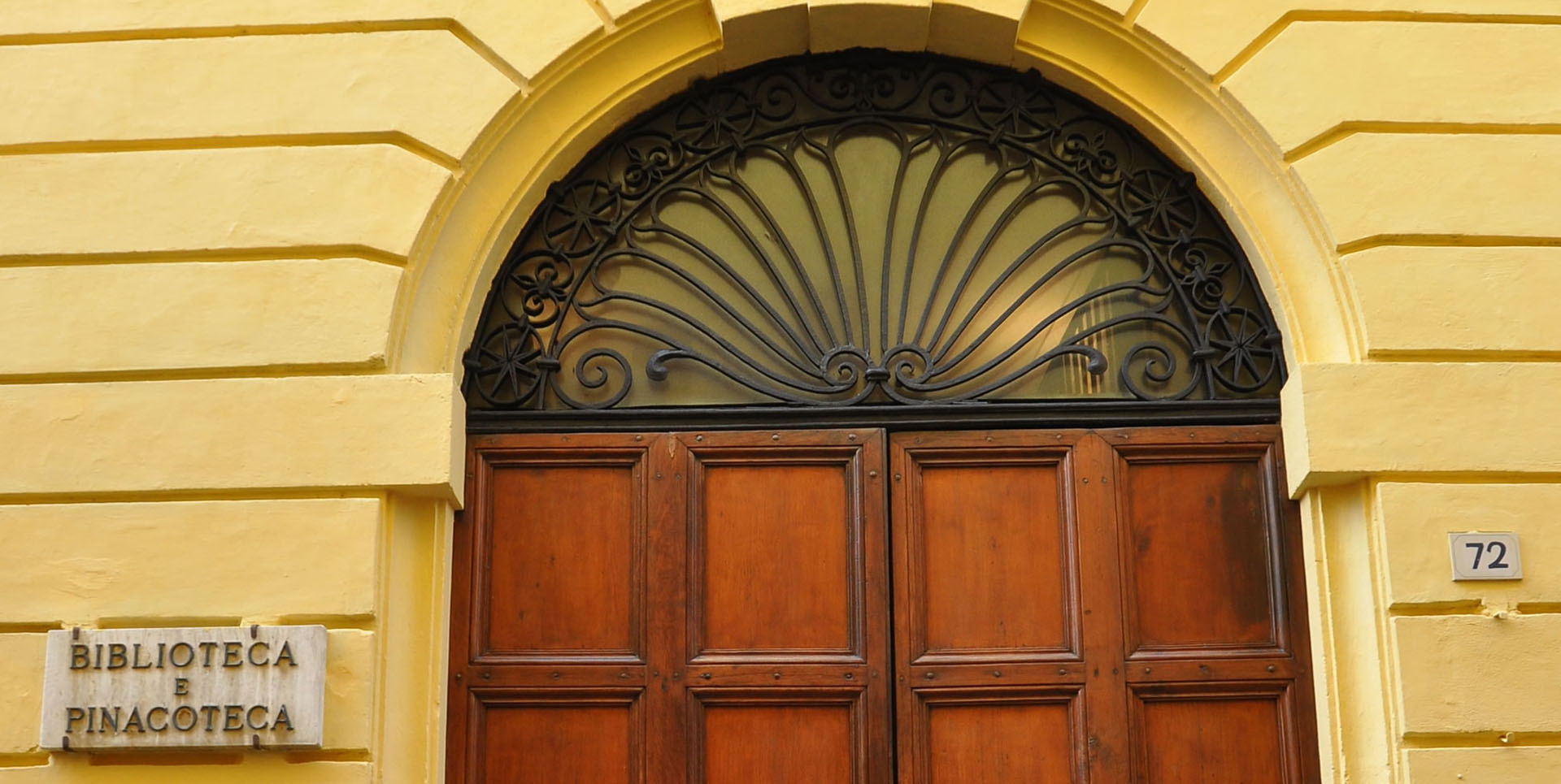 Entrance of the Bevagna Civic Museum at Palazzo Lepri, with wooden doorway and wrought-iron fanlight on an ochre façade.