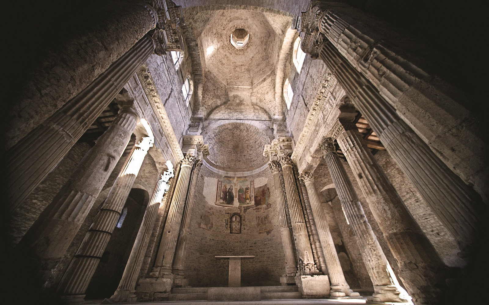 Intérieur de la basilique de San Salvatore à Spolète, avec colonnes antiques, abside ornée de fresques et coupole voûtée.