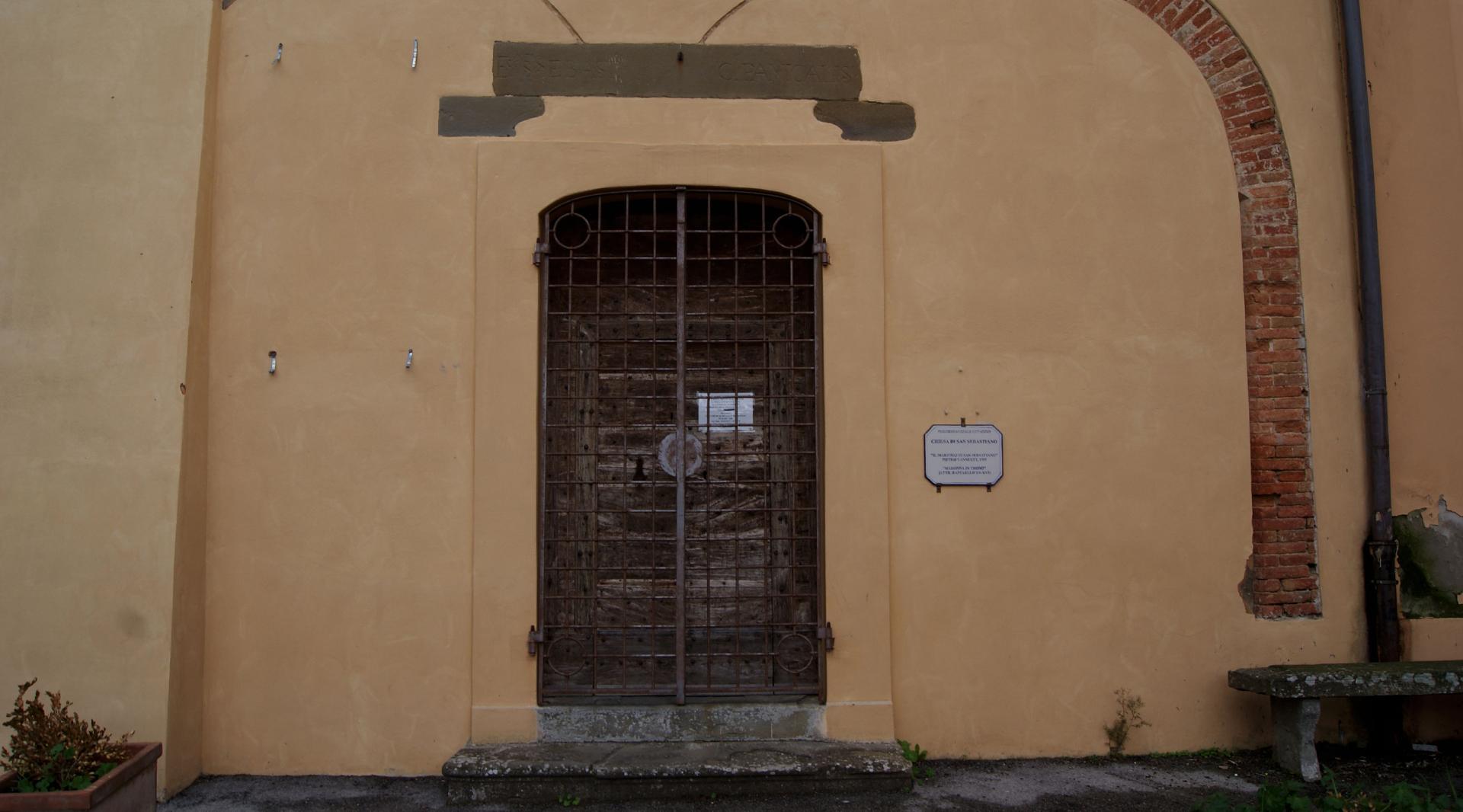 Dettaglio della facciata anteriore della Chiesa di San Sebastiano, rivestita di intonaco. Al centro, un arco in mattoni sovrasta il portone d'ingresso principale