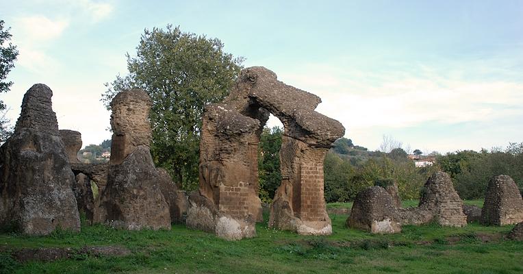 Rovine del teatro romano di Ocriculum, con arcate in muratura circondate da prato e alberi sullo sfondo