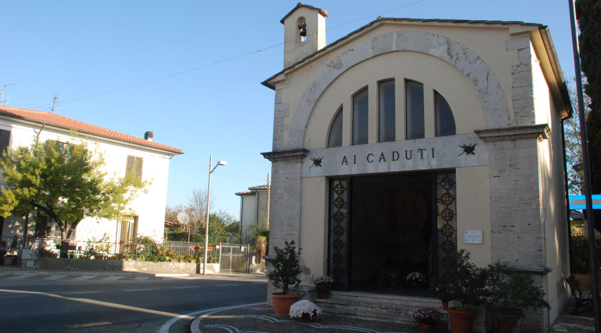 Kapelle San Rocco für die Gefallenen, mit schlichter Fassade, Eingangsportal und kleinem Glockengiebel unter heiterem Himmel.