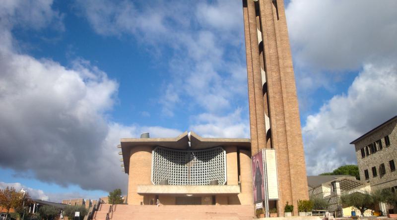Moderne Fassade des Heiligtums von Collevalenza mit einem hohen Ziegelstein-Glockenturm, blauem Himmel und Wolken im Hintergrund.