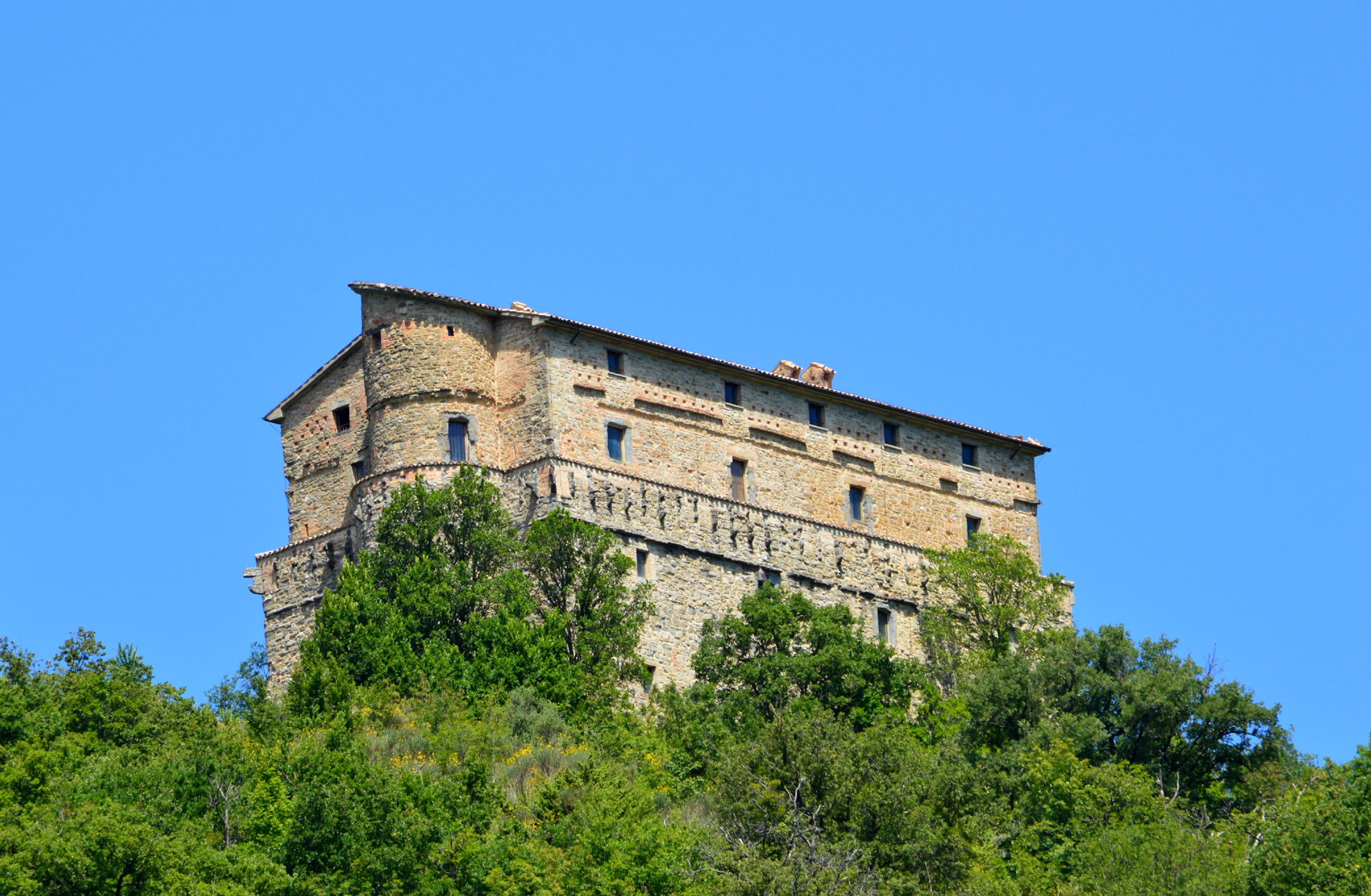 Rocca di Aries a Montone, maestosa fortezza medievale che emerge dalla vegetazione sotto un cielo limpido.