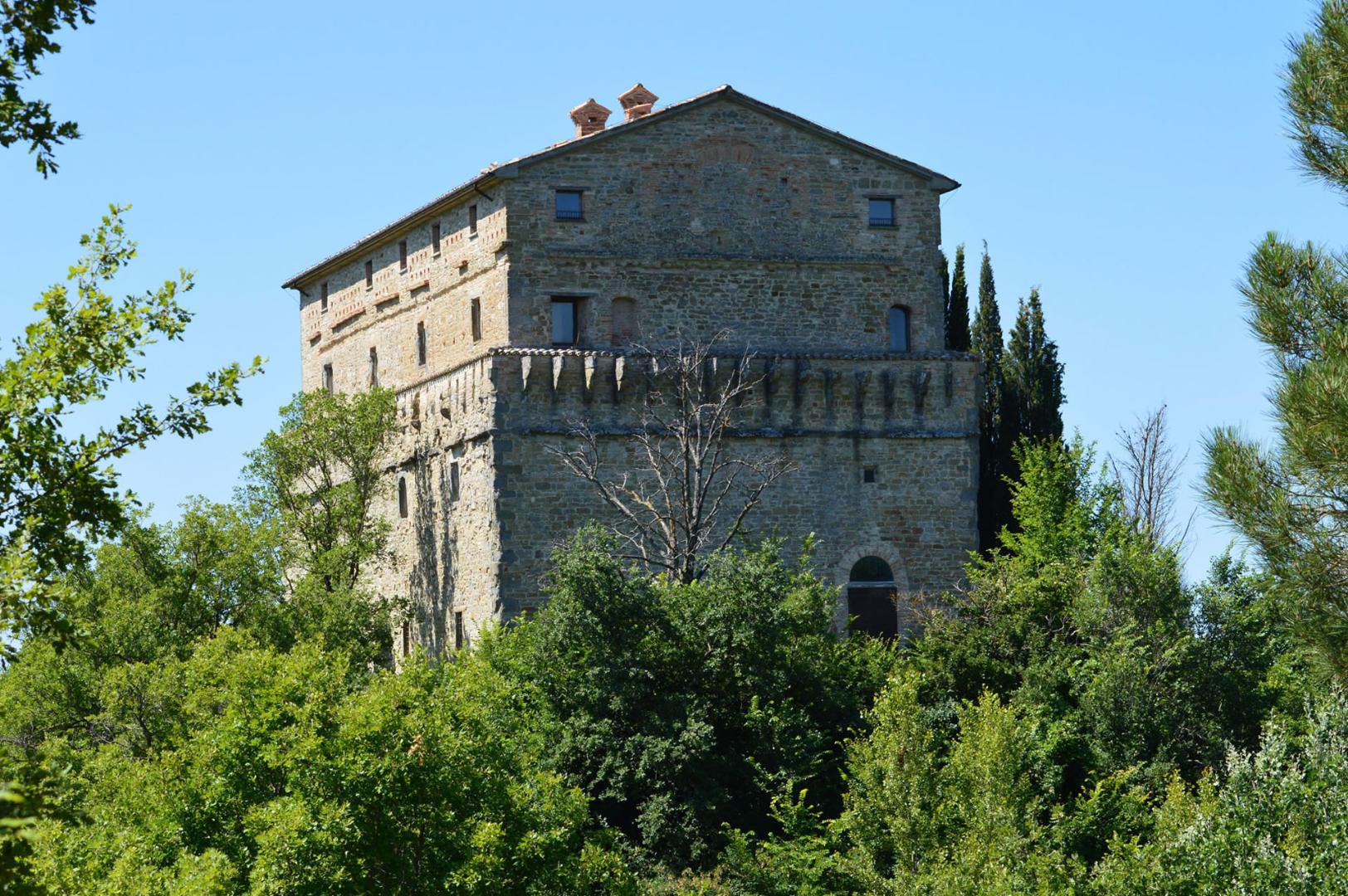 La Rocca di Aries a Montone, imponente edificio in pietra che emerge dal verde della collina sotto un cielo sereno.