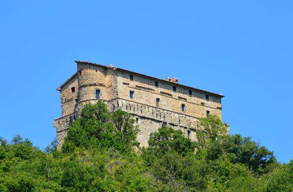  Rocca di Aries in Montone, majestic medieval fortress rising above the vegetation under a clear sky. 