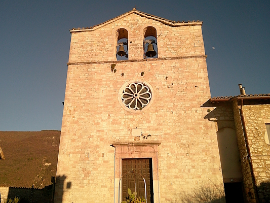 Stone façade of the Church of San Giovanni in Vallo di Nera, featuring a bell gable with two bells and a central rose window.