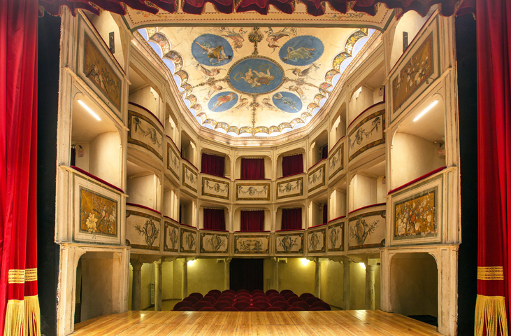 Interior of the Teatro della Concordia in Monte Castello di Vibio, with painted boxes, red curtain and decorated ceiling.