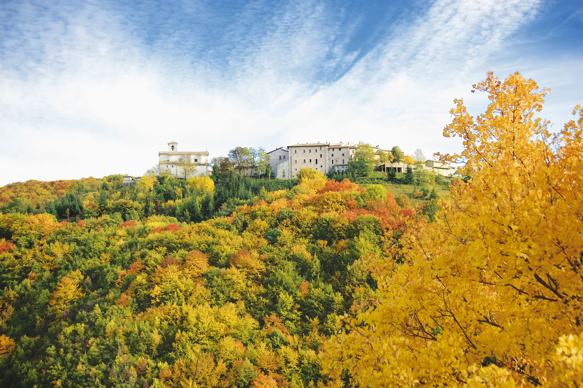 View of Usigni nestled in autumn-colored vegetation. On the left, the Church of San Salvatore can be seen.
