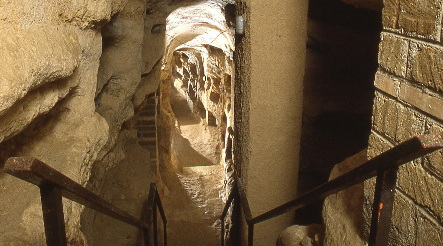 Underground corridor inside the Catacomb of Villa San Faustino. Along the corridor walls, built with a combination of bricks and stone, several burial niches, or loculi, can be seen, stacked on top of each other.