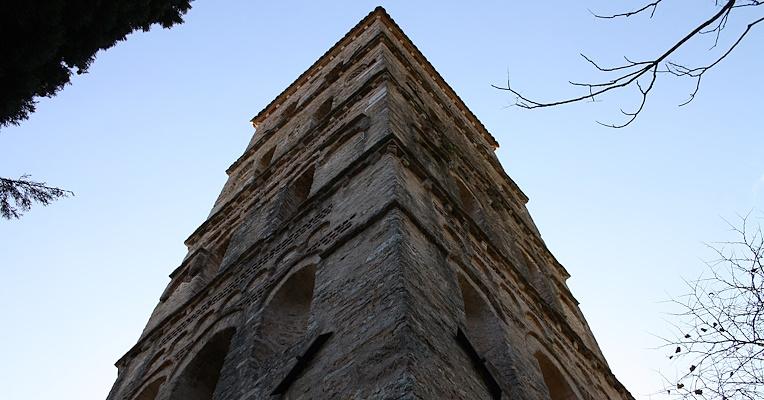 View from below of the bell tower of the Abbey of San Pietro in Valle in Ferentillo, with a clear blue sky in the background. The quadrangular bell tower shows the details of the arched windows and brick cornices.