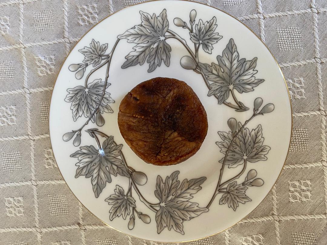 A stuffed dried fig on a porcelain plate decorated with grey fig leaves and a gold rim.
