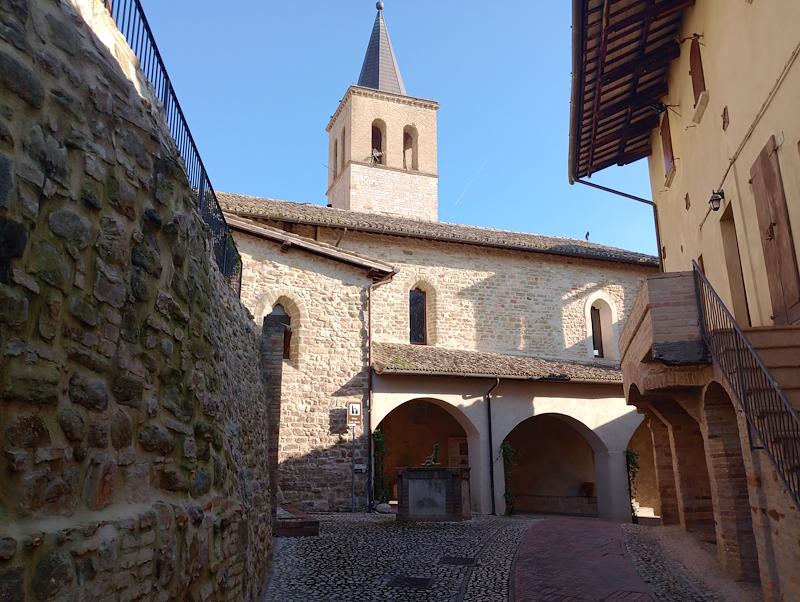 Cobbled alley with a well in front of the porticoed entrance of the Church of Santa Marina, with the bell tower in the background