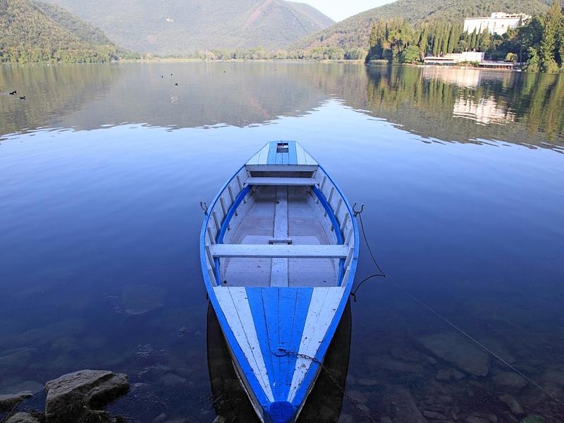 Moored boat on the calm waters of Lake Piediluco with mountains reflected in the background.