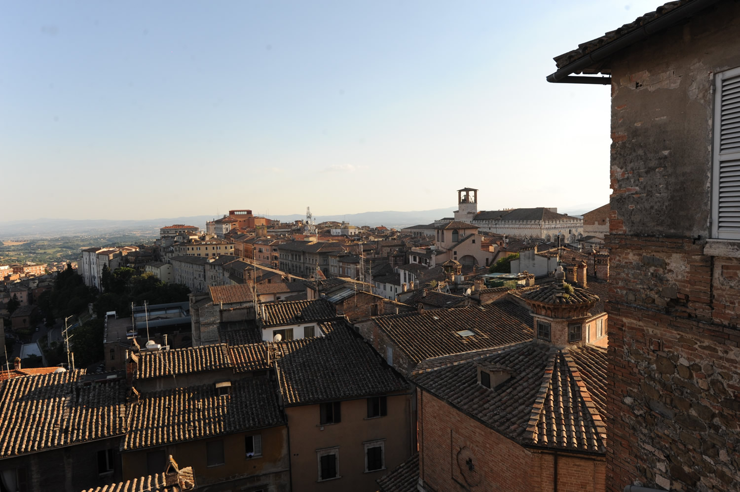 Panorama dei tetti in cotto del centro storico, con edifici medievali e colline sullo sfondo sotto il cielo sereno.
