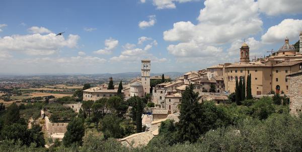 Panorama von Assisi mit historischen Steingebäuden, Glockentürmen und Türmen bei klarem Himmel, aber mit einigen Wolken 