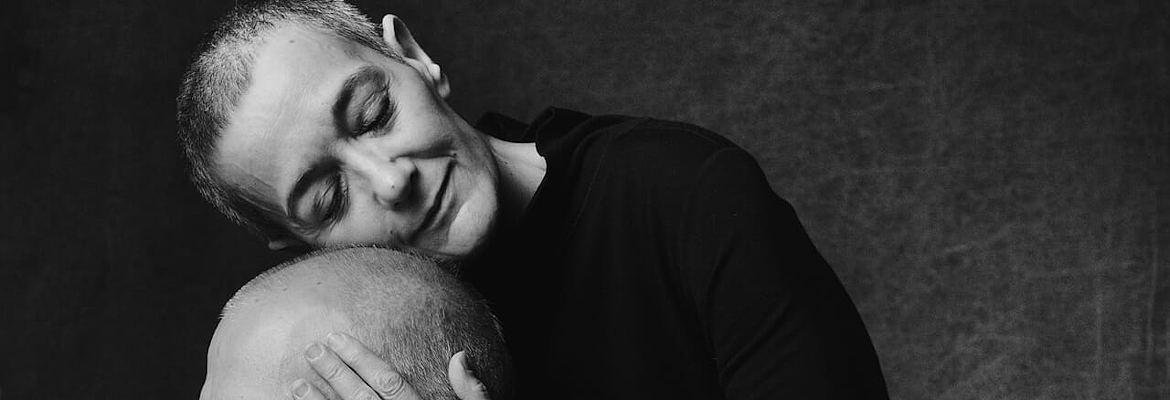 Black-and-white photo of a woman gently embracing a man, both with serene expressions and closed eyes.