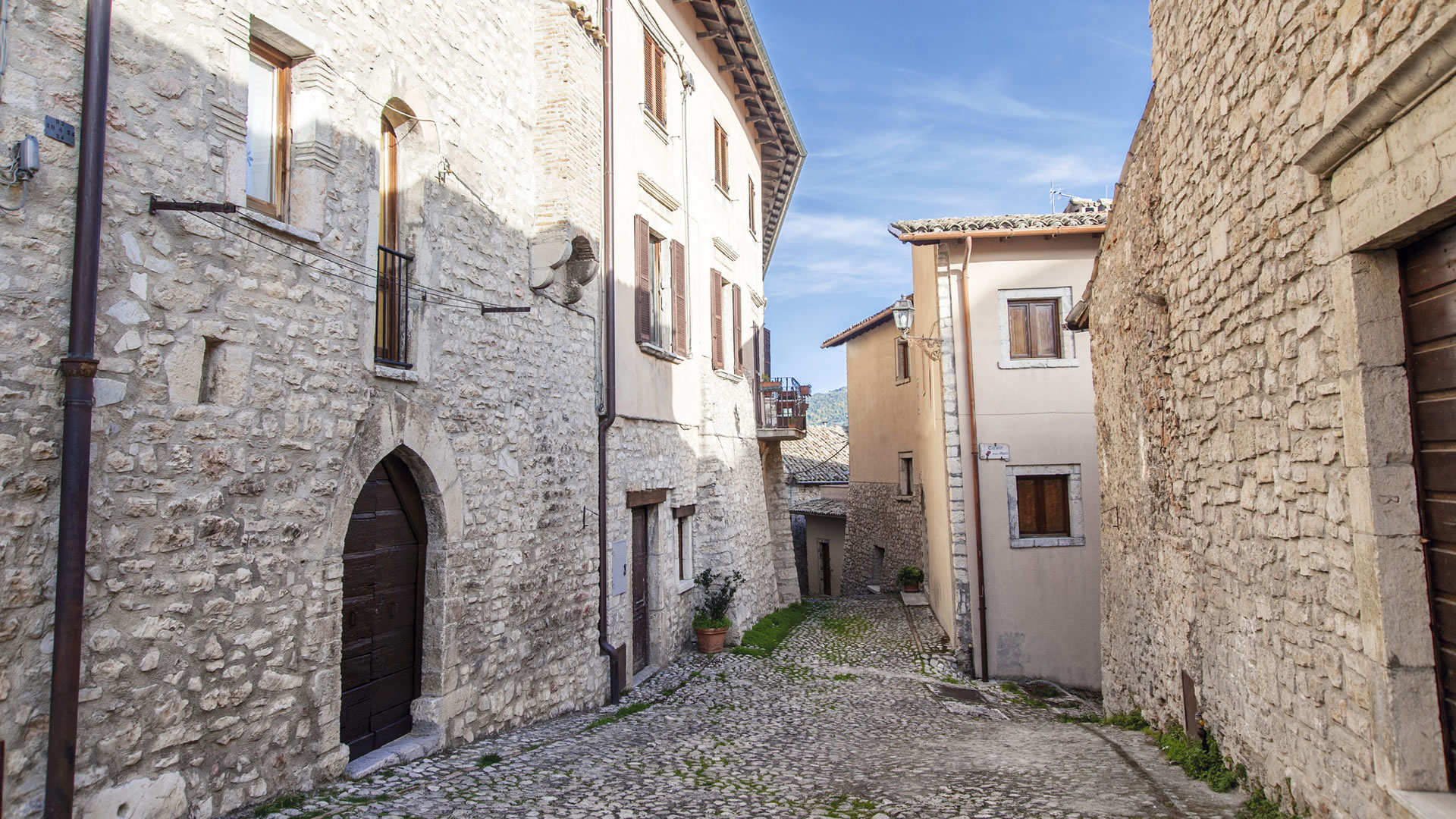 Kopfsteinpflaster-Gasse in Monteleone di Spoleto, gesäumt von Steingebäuden im historischen Zentrum.