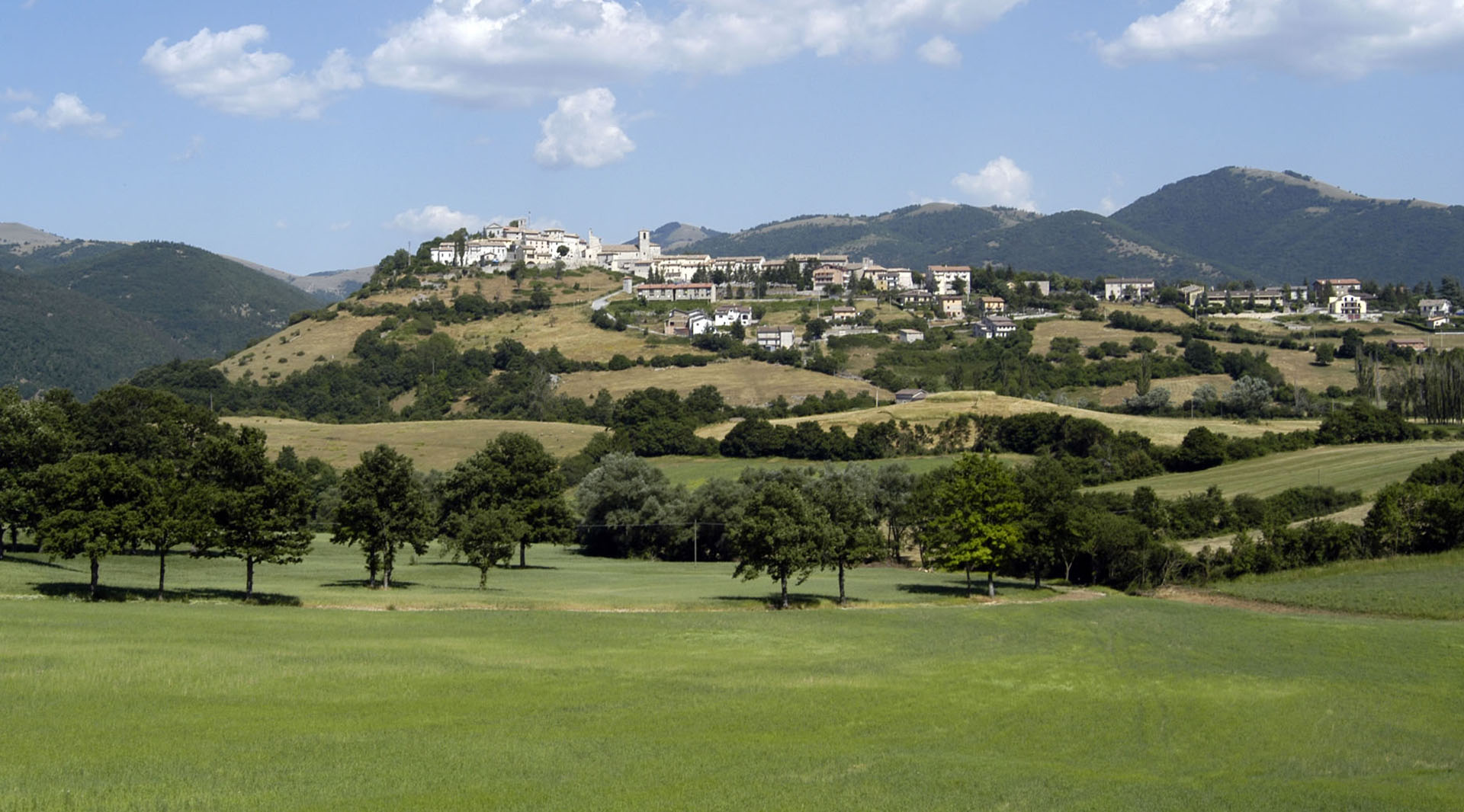 Panorama von Monteleone di Spoleto: Das Dorf liegt auf einem grünen Hügel, umrahmt von Wäldern und den Apenninen.