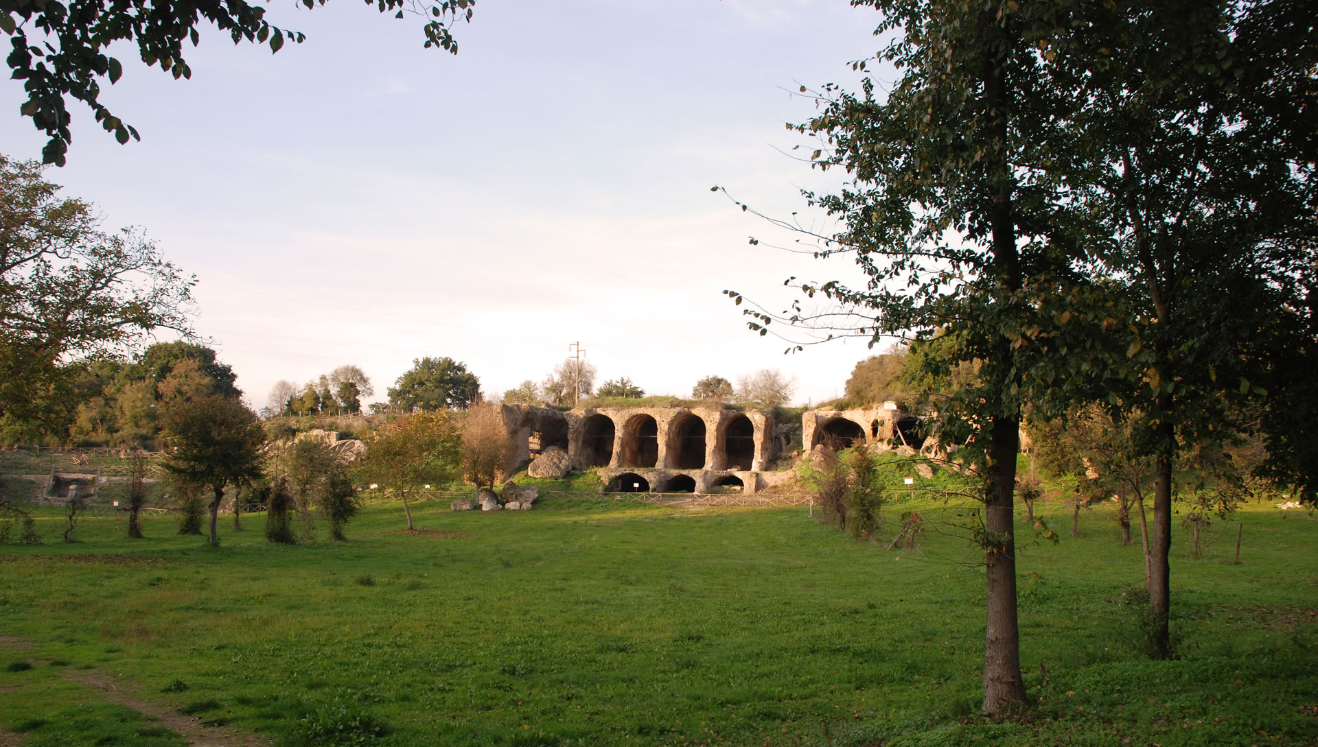 Roman ruins in the archaeological area of Ocriculum, surrounded by greenery in a wide tree-lined meadow.