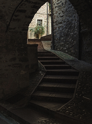 Stone staircase under a medieval arch in Scheggino, overlooking a flowery courtyard and stone walls.