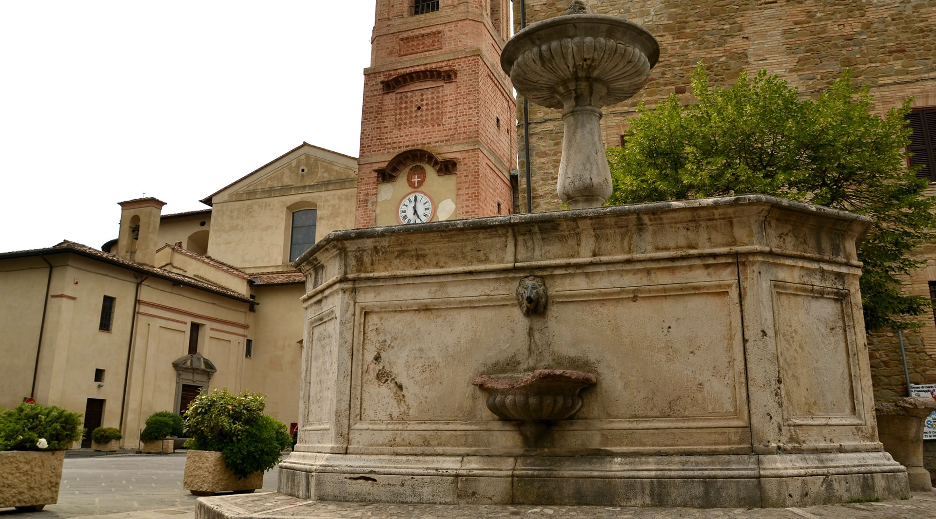 Steinbrunnen auf der Piazza Cavour in Bettona; im Hintergrund der Uhrturm und die Kirche Santa Maria Maggiore.
