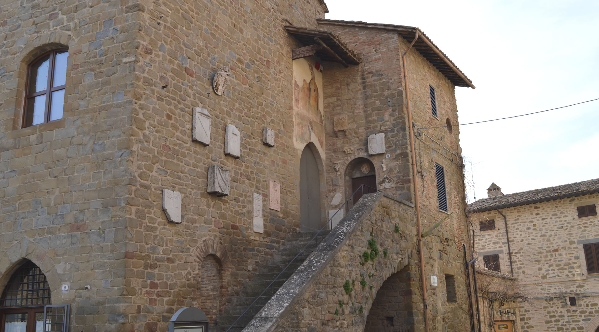 Palazzo del Podestà in Bettona, mittelalterliches Gebäude mit Wappen an der Fassade und Fresko über dem Eingang der Außentreppe.