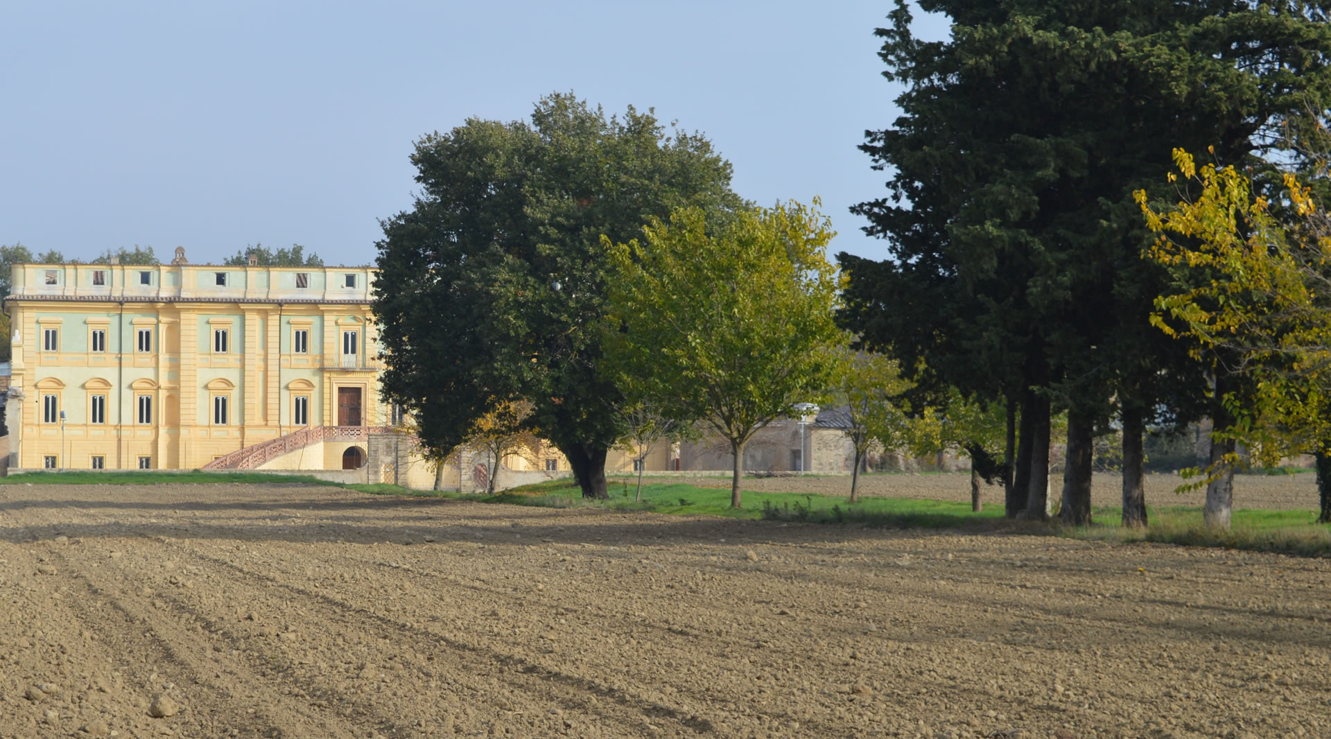 Villa del Boccaglione in Bettona, elegantes Gebäude aus dem 18. Jahrhundert, umgeben von Bäumen und Feldern in der Landschaft.