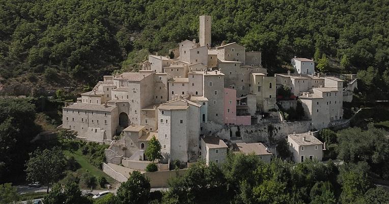 Aerial view of the Castello di Postignano, a hamlet of Sellano, with stone houses perched among the Umbrian woods.