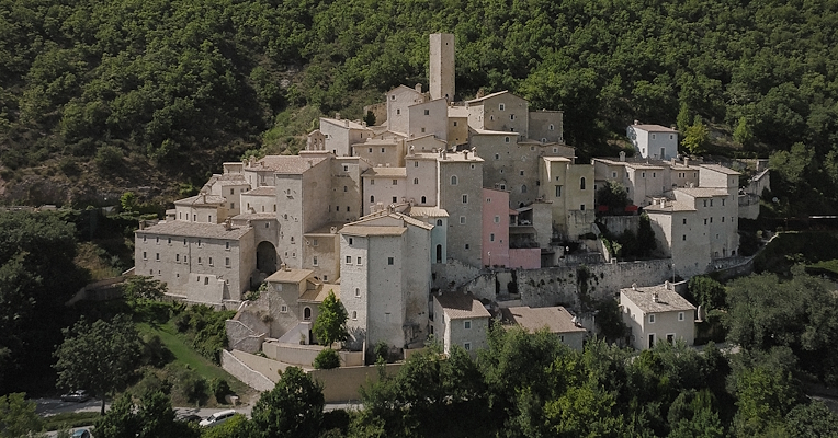 Luftaufnahme der Burg von Postignano, einem Ortsteil von Sellano, mit Steinhäusern, die sich an die umbrischen Wälder schmiegen.