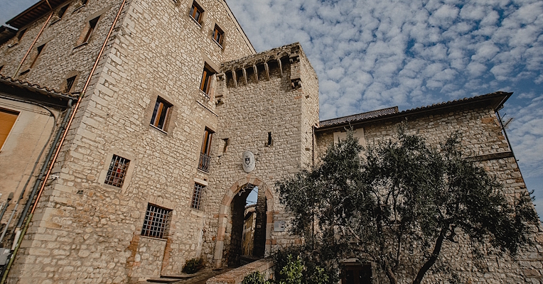 Entrance gate to the village of Montefranco, framed by stone buildings and medieval battlements under a cloudy sky.