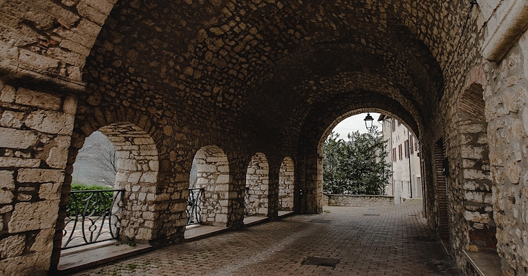 Stone portico in Montefranco with round arches and brick paving, overlooking a street.