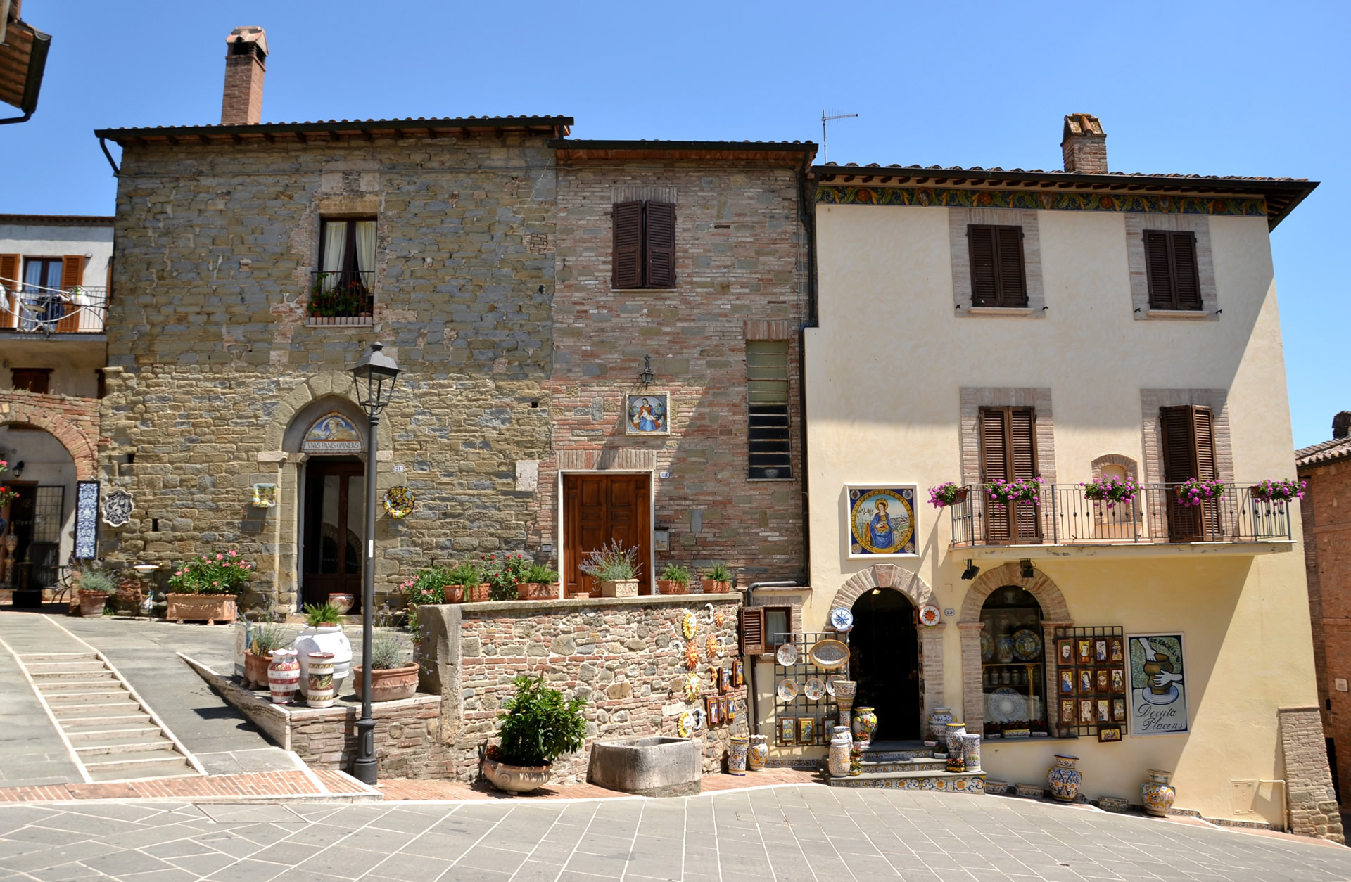 Stone houses and a ceramics shop in Deruta, with a flowered balcony and majolica displayed on the façade.