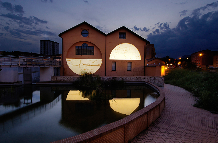 CAOS-Gebäude mit geometrischen Lichtinstallationen, die sich in der Dämmerung im Wasser spiegeln