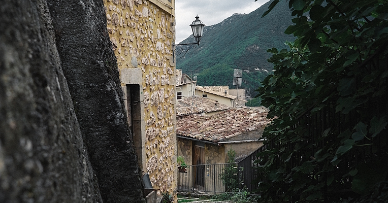 Vicolo di Poggiodomo con case in pietra, tetti in cotto e vista sulle montagne verdi dell’Umbria.