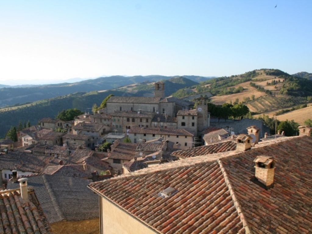 Panoramablick auf Montone mit Terrakottadächern des mittelalterlichen Dorfes, umgeben von grünen Hügeln.
