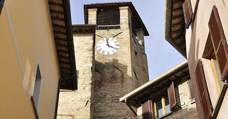 Stadtturm mit Uhr in Montone, eingerahmt von den Dächern und Fassaden der Dorfhäuser.