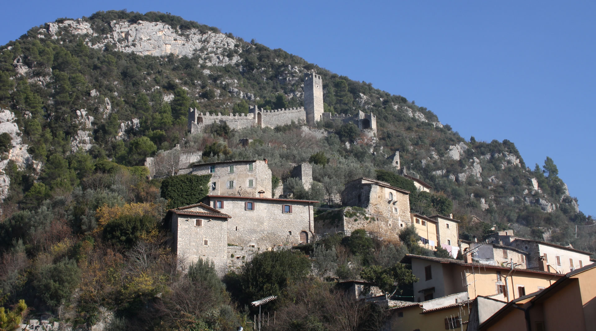 Borgo medievale di Ferentillo arroccato sulla montagna con case in pietra e un castello fortificato tra la vegetazione.