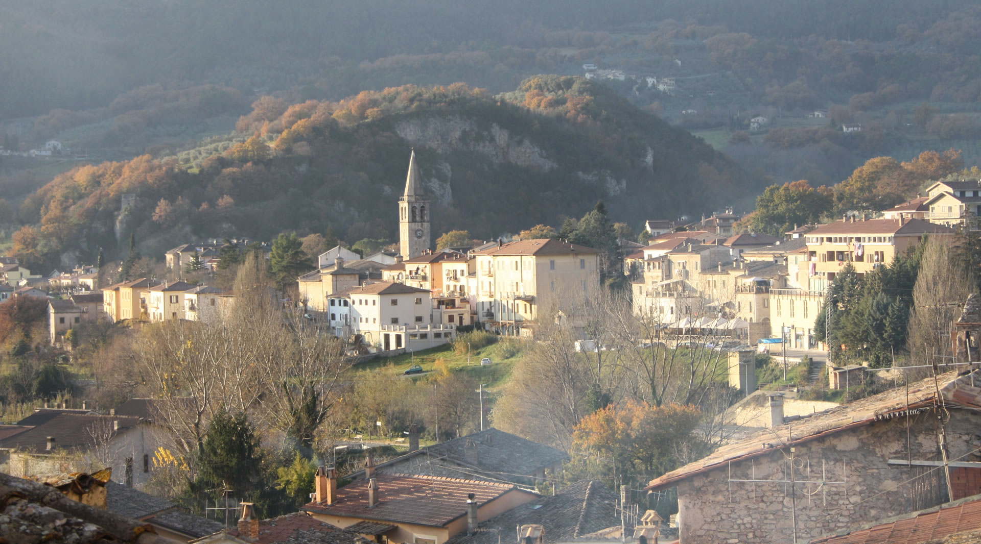 Panorama of Ferentillo, nestled among green hills, with a bell tower rising above the houses bathed in golden light.