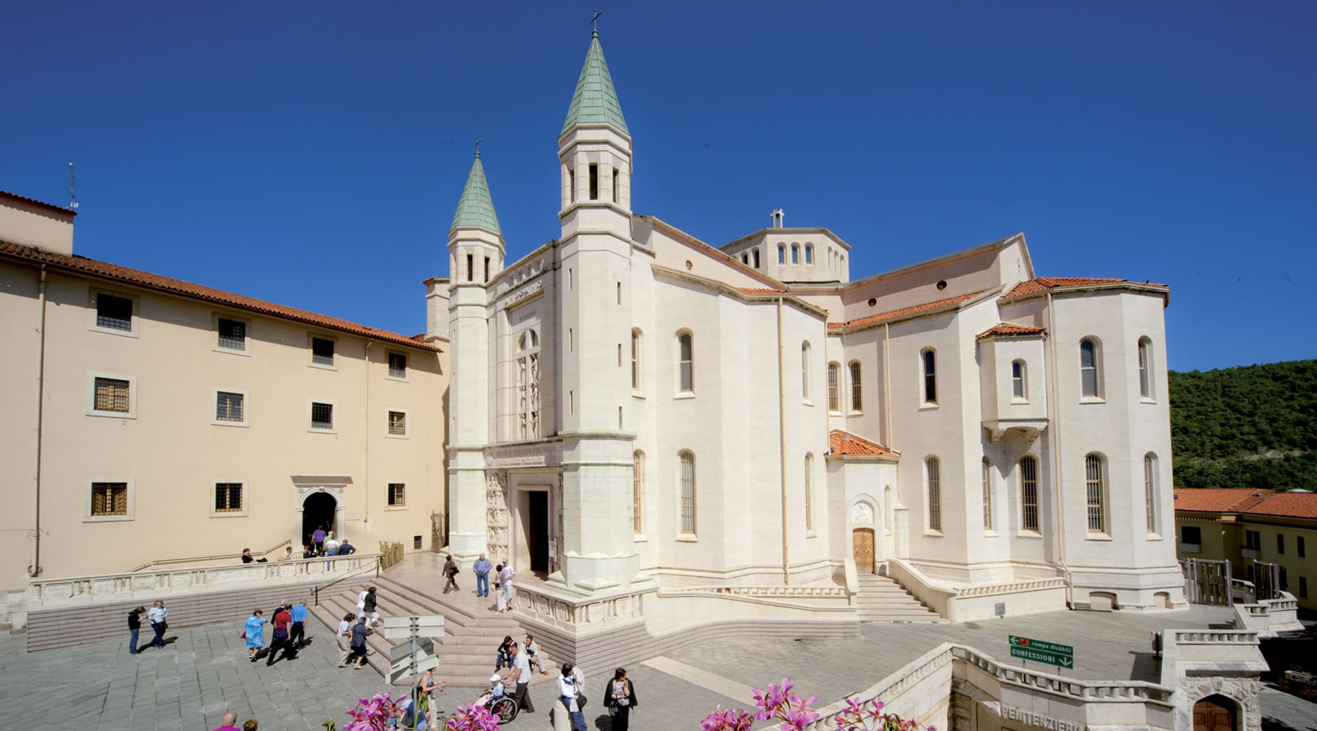 The Basilica of Saint Rita in Cascia, with its twin towers and light-coloured façade, welcomes visitors in the sunlit square.