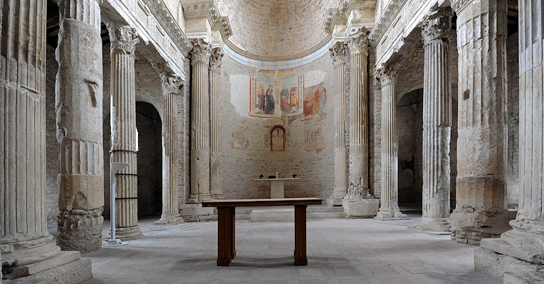 Interno della Basilica di San Salvatore a Spoleto con colonne romane, abside con affreschi e altare centrale.