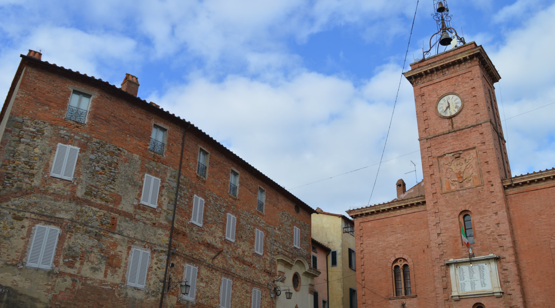 Uhrturm von Monteleone di Orvieto aus roten Ziegeln mit verzierter Fassade, neben historischen Gebäuden.