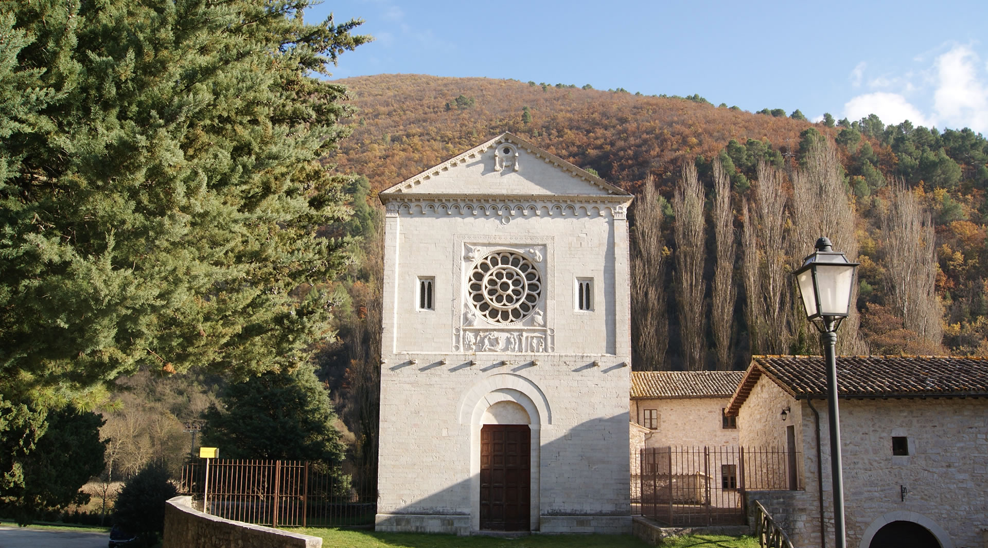 Romanische Fassade der Abtei der Heiligen Felice und Mauro, eingebettet in das Grün des Valnerina-Tals am Fuße der Hügel.