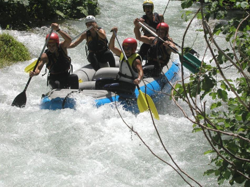 Cinque ragazzi su un gommone, con caschi e giubbotti salvagente, fanno rafting sul fiume Nera, fra schizzi e vegetazione fitta