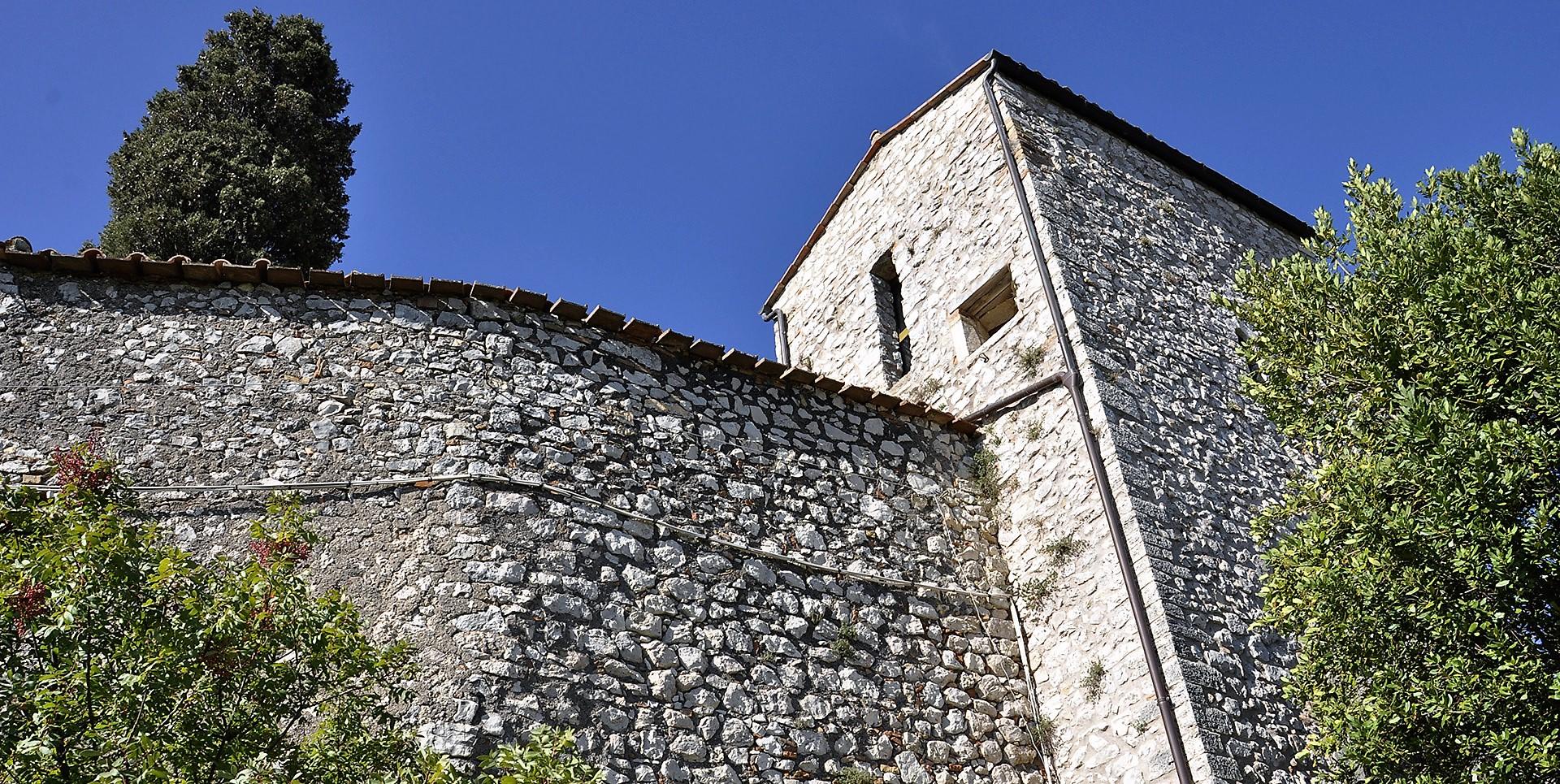 Torre angolare in pietra del Castello del Poggio con mura fortificate e cielo limpido sullo sfondo.