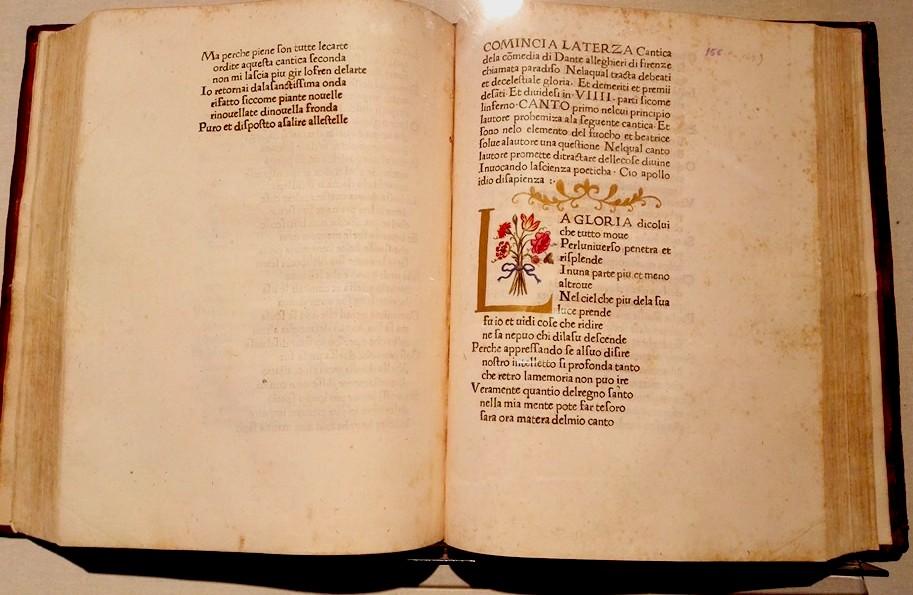 Antico manoscritto della Divina Commedia aperto, con iniziale decorata e dettagli ornamentali dorati.