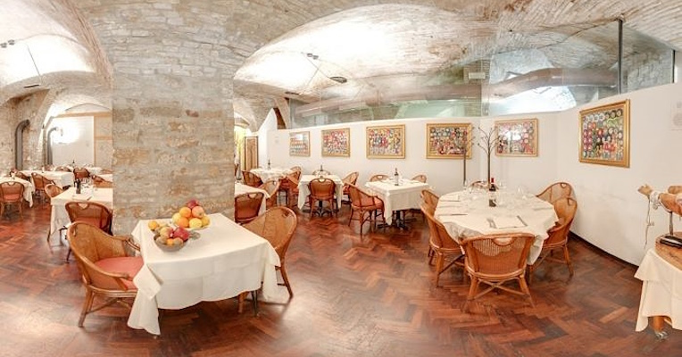 Restaurantzimmer mit gewölbter Steindecke, Gemälden an den Wänden, Holzboden und gedeckten Tischen.