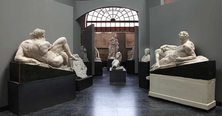 Museumssaal mit Gipsfiguren klassischer Werke und Büsten, erleuchtet durch ein großes zentrales Bogenfenster.